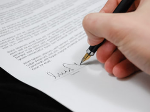 hand holding pen signing his name on signature line